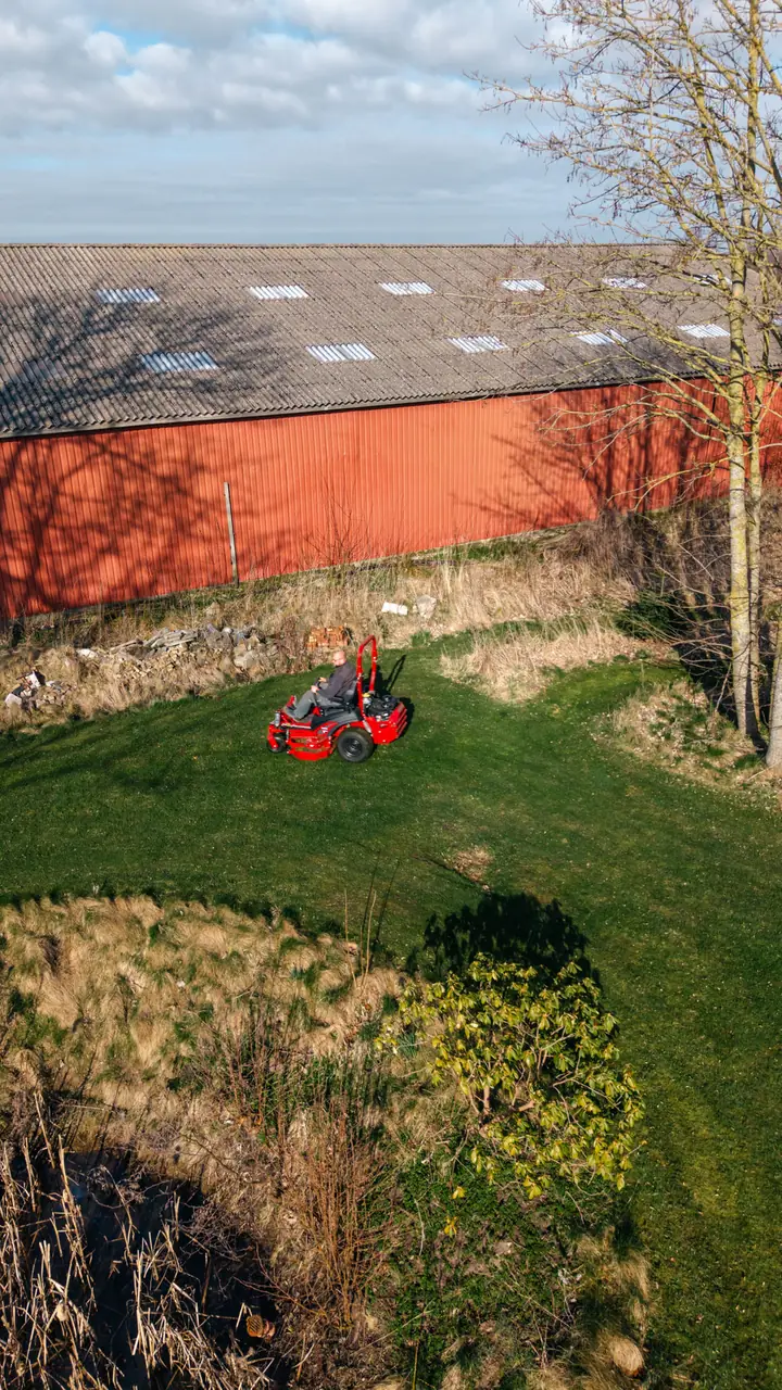 Luftfoto af græsslåning på en plæne ved en rød lade